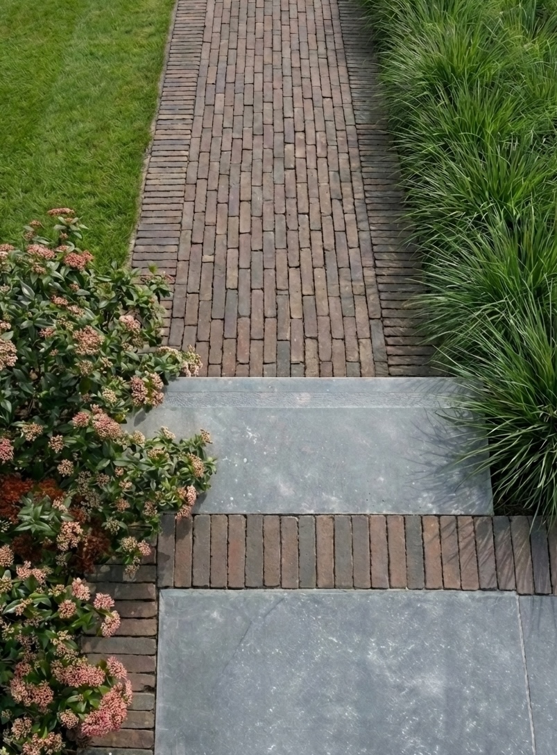 Klinkerpad met blauwe hardsteen, siergrassen en Skimmia